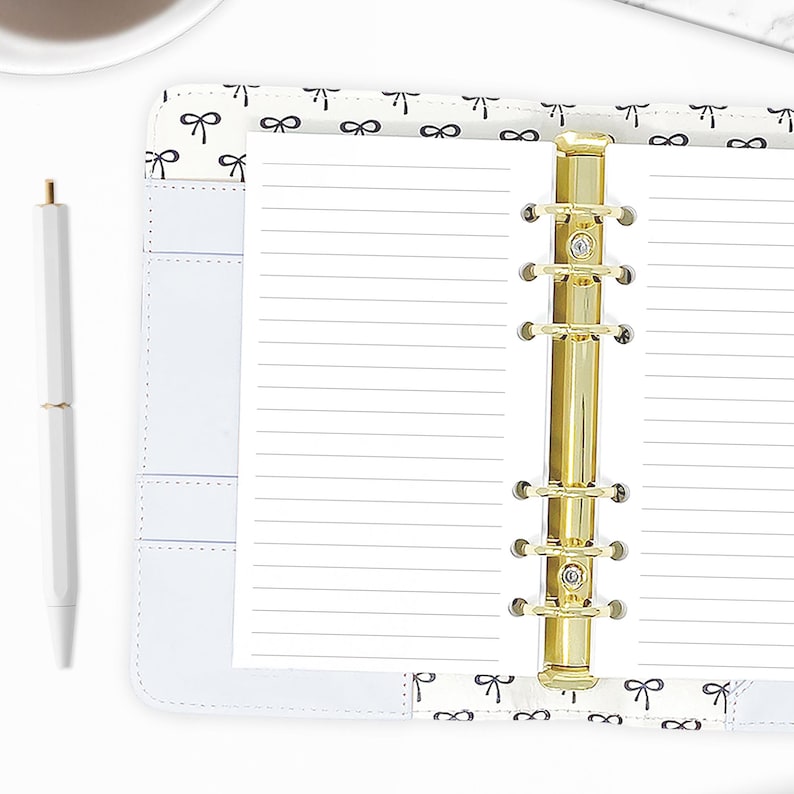 Personal lined paper planner refills shown in a ring binder, gold rings open across two horizontally lined pages, styled with a white pen on a bow-print desktop. Hand-cut and bound in our small studio. Physical refills only no binder or accessories included.