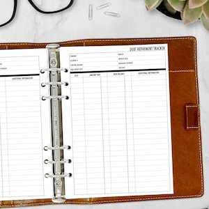 A5 debt repayment tracker planner insert open inside a leather ring binder with glasses showing payment columns and balance tracking detail, physical refills only no binder or accessories included