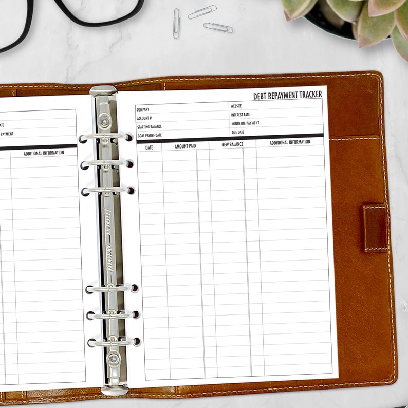 A5 debt repayment tracker planner insert open inside a leather ring binder with glasses showing payment columns and balance tracking detail, physical refills only no binder or accessories included