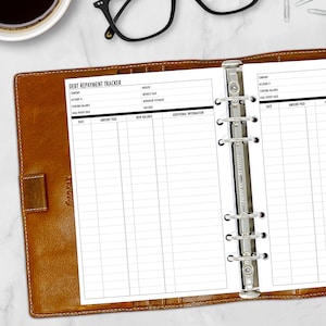 May include: A black and white debt repayment tracker with a brown leather binder. The tracker has columns for company, account number, starting balance, goal payoff date, date, amount paid, new balance, and additional information.