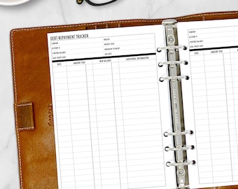 May include: A black and white debt repayment tracker with a brown leather binder. The tracker has columns for company, account number, starting balance, goal payoff date, date, amount paid, new balance, and additional information.