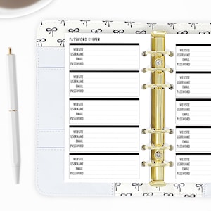 Personal password keeper planner refills shown in a ring binder, gold rings open across a two-page spread with rows of Website, Username, Email, and Password fields, styled with a white pen on a bow-print desktop. Hand-cut and bound in our small studio. Physical refills only no binder or accessories included.