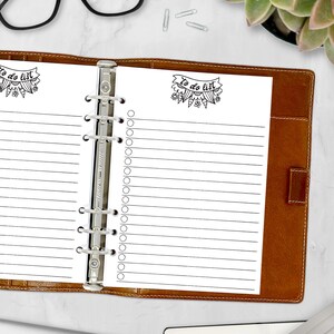 May include: Open brown leather binder with lined paper. The paper has the words "To do list" in a banner at the top, with a floral design. The binder is open, revealing the lined pages, and is on a white surface.