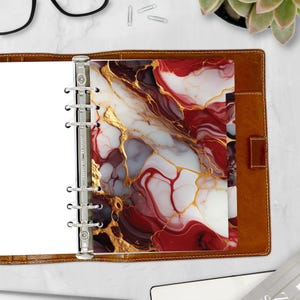 May include: A brown leather planner with a silver binder and a red, white, and gold marble design insert. The insert has a swirling pattern of red, white, and gold.