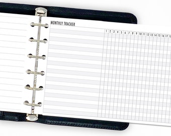 Puede incluir: Agenda abierto en una página "MONTHLY TRACKER". La página presenta una cuadrícula para el seguimiento mensual, con los números del 1 al 18 en la parte superior. El planificador es negro con una encuadernación plateada.