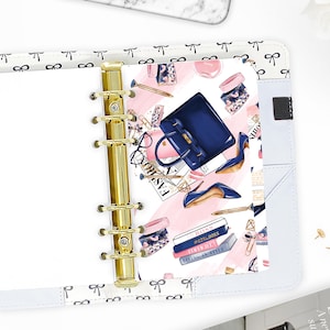 May include: A planner with a gold binder and a decorative insert featuring a navy blue handbag, high heels, and the text "FASHION". The insert has a pink and white background with illustrations of accessories.
