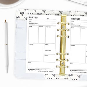 May include: A white planner with a gold ring binder. The planner has a black and white bow pattern and the text "Bible Study" on the front. The planner has sections for passage, theme, written by and for whom, outline, word study, observations, application, key verses, supporting verses, questions, and prayer.