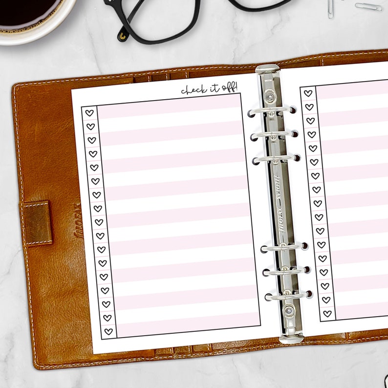 Printed A5 Check It Off checklist planner insert in Bubblegum shown in a tan leather ring binder on a marble desk with coffee and glasses. Pink striped design with heart checkboxes and Check It Off script header. Physical paper insert only -- binder and accessories not included. Planner insert is made in the USA by CityGirl Planners.
