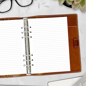 May include: Open brown leather binder with lined white paper. The binder has a silver metal ring mechanism and a magnetic closure. The paper is ready for notes, lists, or journaling. The binder is on a white surface.