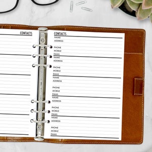 May include: A brown leather binder with a silver metal clasp, open to reveal a contact list. The contact list has the word "CONTACTS" at the top, followed by fields for name, address, phone, mobile, and email. The binder is on a white marble surface.