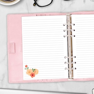May include: A light pink leather personal organizer with a six-ring metal binder mechanism. The interior features white lined paper with a small floral illustration in the bottom left corner, displaying orange and peach-colored flower petals.