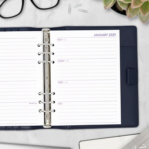 May include: Open planner with a navy blue cover and lined pages. The pages are open to January 202? with the days of the week and space for notes. Silver binder rings and paper clips are visible.