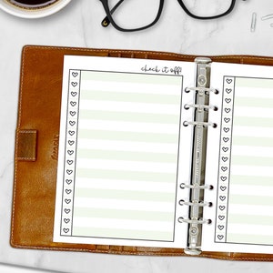 Printed A5 Check It Off checklist planner insert in Celery shown in a tan leather ring binder on a marble desk. Green striped design with heart checkboxes. Physical paper insert only -- binder and accessories not included. Planner insert is made in the USA by CityGirl Planners.