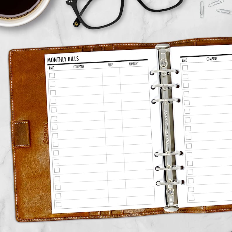 Printed A5 monthly bill tracker insert shown in a tan leather ring binder planner. Columns for company, due date, amount, and paid checkbox. Physical paper insert only — binder not included.