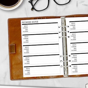 May include: A brown leather bound notebook with a silver ring binder. The notebook is open to a page with the title "PASSWORD KEEPER" and has multiple sections for website, username, email, and password.