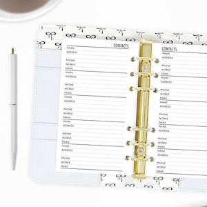 May include: A white contact book with a gold binder and a white and black bow pattern. The book has pages for writing down contact information, including name, address, phone number, mobile number, and email address.