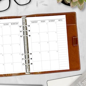 A5 tan ring binder open on a white desk displaying the monthly calendar inserts alongside a keyboard, black coffee mug, glasses, and succulent. A5 planner inserts made in the USA by CityGirl Planners.