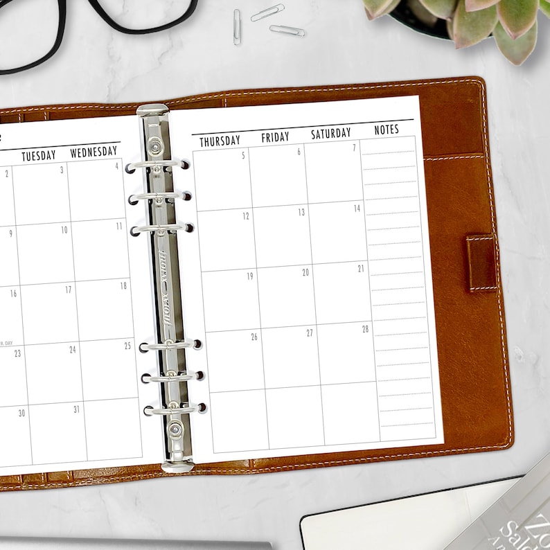 A5 tan ring binder open on a white desk displaying the monthly calendar inserts alongside a keyboard, black coffee mug, glasses, and succulent. A5 planner inserts made in the USA by CityGirl Planners.