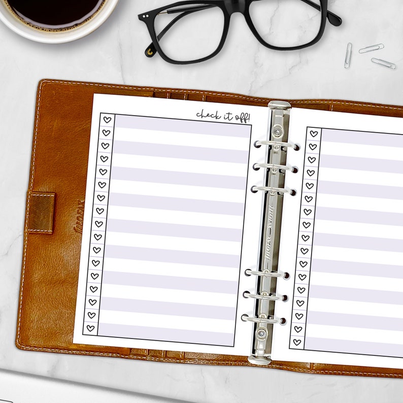 Printed A5 Check It Off checklist planner insert in Lavender shown in a tan leather ring binder on a marble desk. Purple striped design with heart checkboxes. Physical paper insert only -- binder and accessories not included. Planner insert is made in the USA by CityGirl Planners.