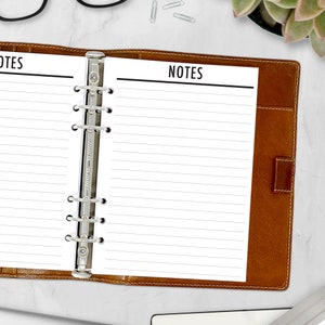May include: A brown leather bound notebook with a silver binder and lined pages. The notebook is open to a page with the word "NOTES" printed at the top.