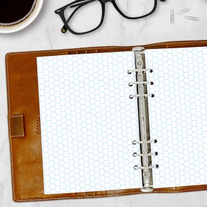 May include: A brown leather bound planner with a silver ring binder. The planner is open to a page with a light blue hexagonal grid pattern.