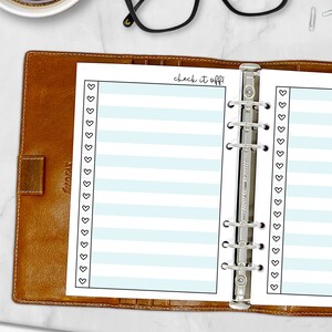 Printed A5 Check It Off checklist planner insert in Sky shown in a tan leather ring binder on a marble desk. Blue striped design with heart checkboxes. Physical paper insert only -- binder and accessories not included. Planner insert is made in the USA by CityGirl Planners.