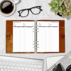 Open A5 Debt Repayment Tracker refill insert in a tan leather six-ring binder on a white marble desk. Two-page spread with DEBT REPAYMENT TRACKER header, account fields, and a payment log. Styled flatlay with a cup of black coffee, black eyeglasses, a succulent in a pink pot, a white keyboard, and a magazine. Physical paper insert only -- binder and accessories not included. Planner insert is made in the USA by CityGirl Planners