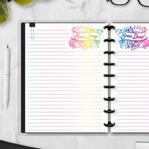 May include: Open notebook with lined pages and a black binding. The pages have a rainbow gradient along the edges. The words "Brain Dump" are written in a colorful banner on the top right and left pages. A white pen is visible on the left.