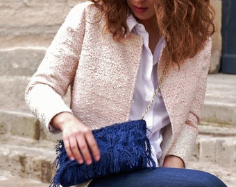 May include: A woman wearing a pink tweed jacket, a white shirt, and blue jeans is holding a blue fringed clutch bag.