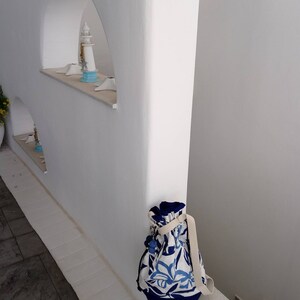 May include: A white wall with a blue and white patterned bag hanging on a ledge. The bag has a white strap and a drawstring closure.