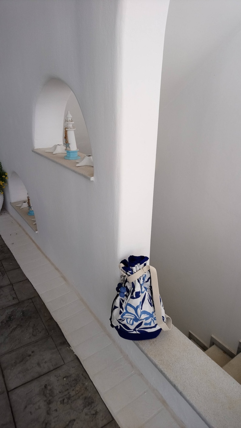 May include: A white wall with a blue and white patterned bag hanging on a ledge. The bag has a white strap and a drawstring closure.