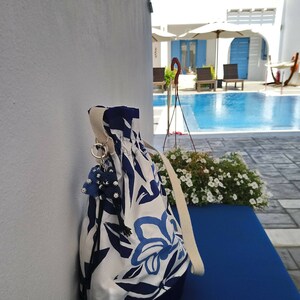 May include: A white and blue floral print drawstring bag with a navy blue bottom. The bag has a white strap and a small blue and white charm attached to it.
