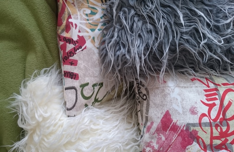 Puede incluir: Tres almohadas decorativas con diferentes patrones. Una almohada es blanca con una textura esponjosa, otra es gris con una textura esponjosa y la tercera es blanca con un dise&ntilde;o de estilo graffiti colorido.