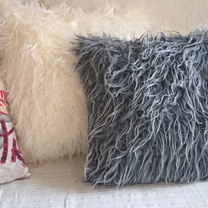 Puede incluir: Tres almohadas decorativas, una con textura esponjosa blanca, otra con textura esponjosa gris y una con un patr&oacute;n de graffiti colorido.