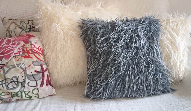 Puede incluir: Tres almohadas decorativas, una con textura esponjosa blanca, otra con textura esponjosa gris y una con un patr&oacute;n de graffiti colorido.