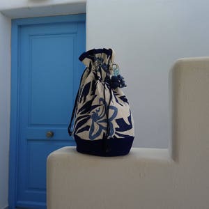 May include: A white drawstring bag with a blue floral pattern and a blue trim. The bag is sitting on a white surface in front of a blue door.