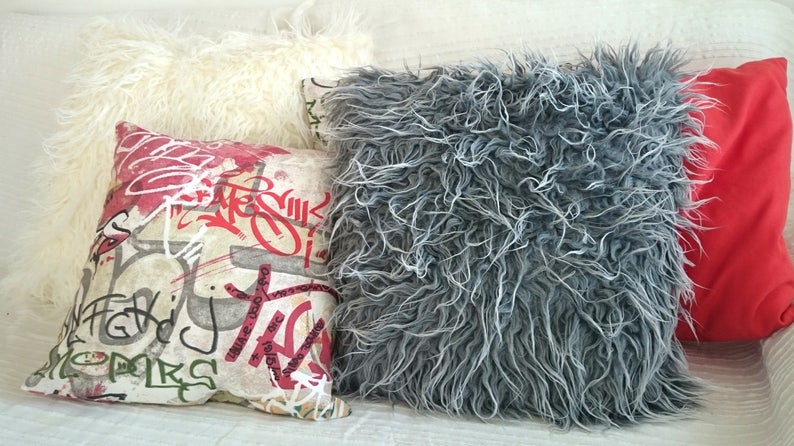 Puede incluir: Cuatro almohadas decorativas con diferentes texturas y patrones. Una almohada es blanca y esponjosa, otra es gris y esponjosa, una es roja y la &uacute;ltima es beige con letras de estilo graffiti rojo y negro.