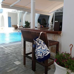 May include: A blue and white patterned drawstring bag hanging on a brown wicker chair by a swimming pool. The chair is on a patio with a white tiled floor.