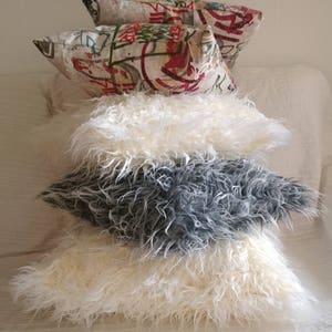 Puede incluir: Un conjunto de cuatro almohadas decorativas. Las dos almohadas superiores est&aacute;n hechas de una tela estampada con fondo blanco y dise&ntilde;os coloridos. Las dos almohadas inferiores est&aacute;n hechas de piel sint&eacute;tica blanca y gris esponjosa.