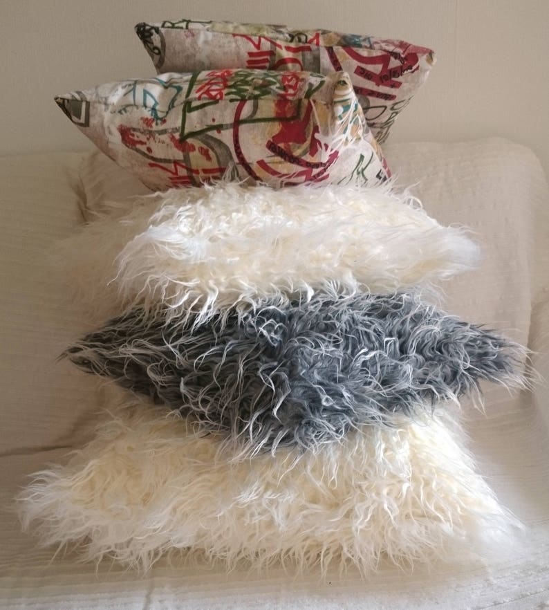 Puede incluir: Un conjunto de cuatro almohadas decorativas. Las dos almohadas superiores est&aacute;n hechas de una tela estampada con fondo blanco y dise&ntilde;os coloridos. Las dos almohadas inferiores est&aacute;n hechas de piel sint&eacute;tica blanca y gris esponjosa.