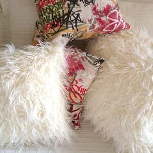 Puede incluir: Dos almohadas blancas y esponjosas con una almohada estampada de colores encima. La almohada estampada es roja, blanca y negra con dise&ntilde;os abstractos.
