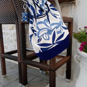 May include: A white and blue floral patterned drawstring bag with a blue trim hanging on a brown wicker chair. The bag has a blue and white charm attached to it.
