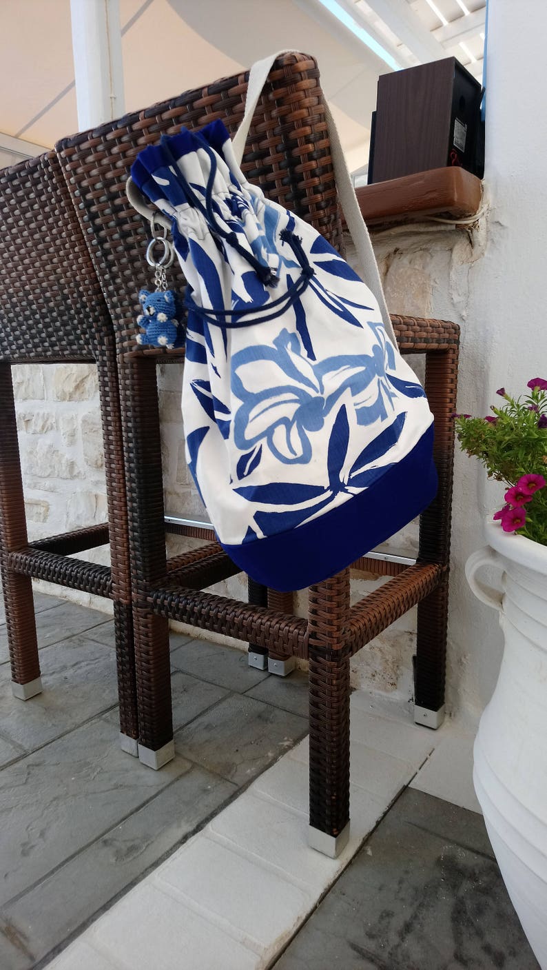 May include: A white and blue floral patterned drawstring bag with a blue trim hanging on a brown wicker chair. The bag has a blue and white charm attached to it.