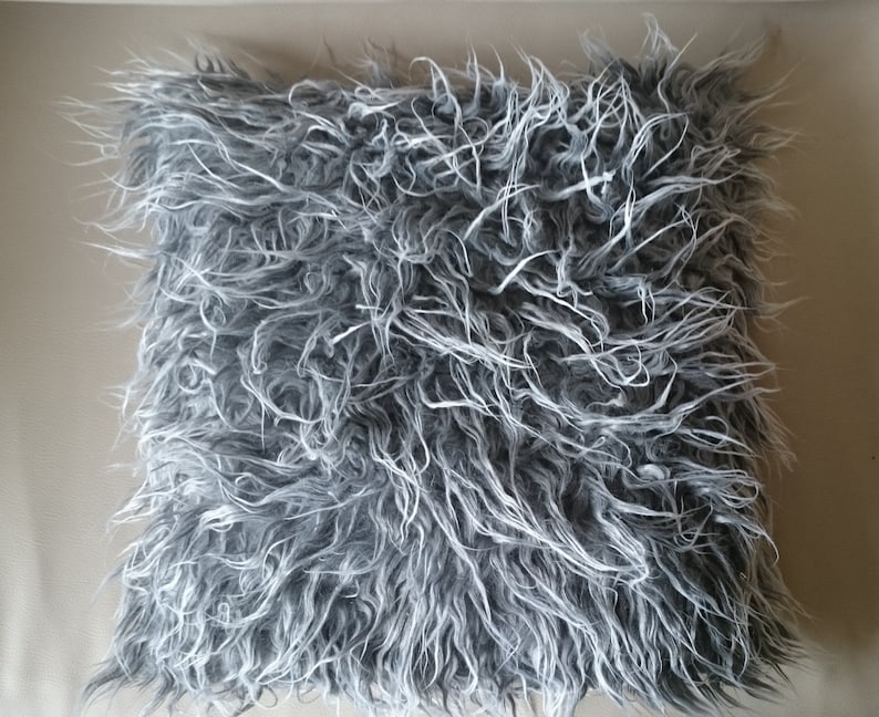 Puede incluir: Una almohada gris y blanca esponjosa con una textura suave y afelpada. La almohada est&aacute; hecha de piel sint&eacute;tica y es perfecta para agregar un toque de comodidad y estilo a cualquier habitaci&oacute;n.