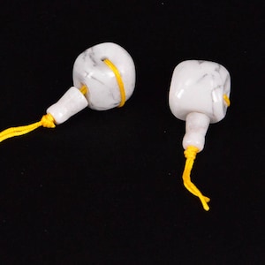 May include: Two white marble prayer beads with yellow string tassels. The beads are round and have a smooth, polished finish.