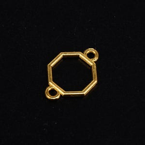 Op de afbeelding: Goudkleurige metalen achtekkig connector met twee springringen. De connector is ontworpen voor het maken van sieraden.