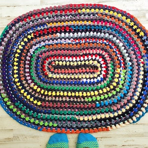 May include: Oval rag rug in a variety of colors, including red, blue, green, and yellow. The rug is handmade with a repeating pattern of fabric strips. The rug is on a light wood floor.