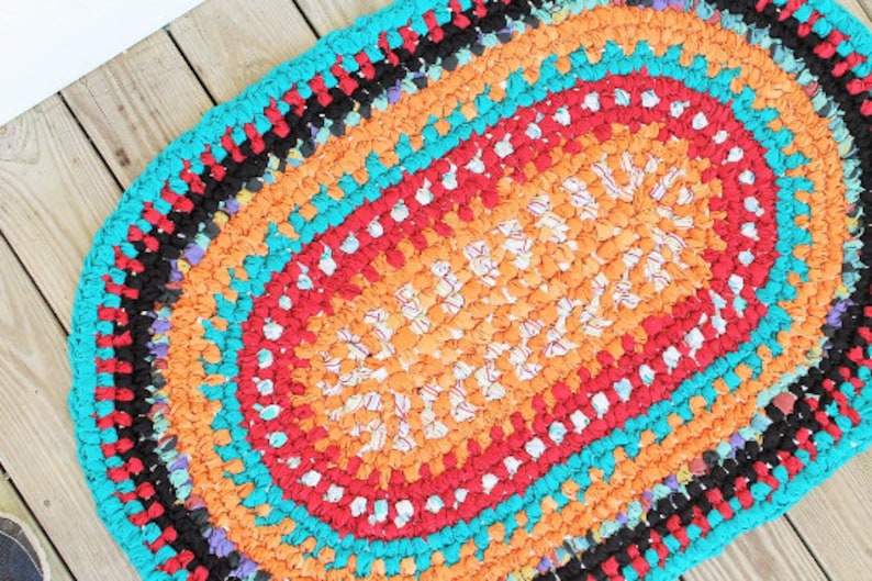 May include: A colorful oval rug made from crocheted fabric scraps in shades of orange, red, turquoise, and black.