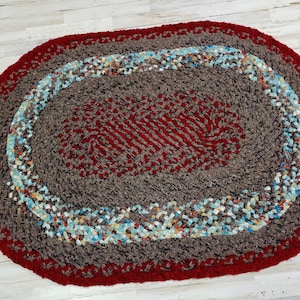 May include: A brown and red oval braided rug with a blue and white braided border.