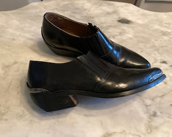 Peut inclure: Une paire de bottes de cowboy en cuir noir avec des bouts pointus et des accents argentés. Les bottes ont un talon bas et une conception à enfiler.
